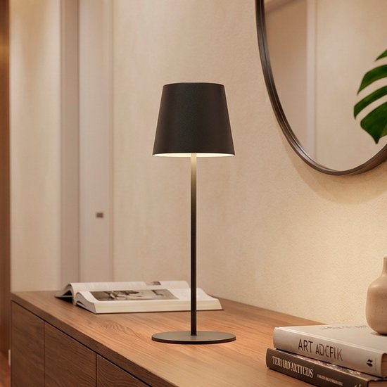 Lampe de table anthracite avec abat-jour conique sur une base ronde et élancée. Posée sur un meuble en bois à côté de livres.
