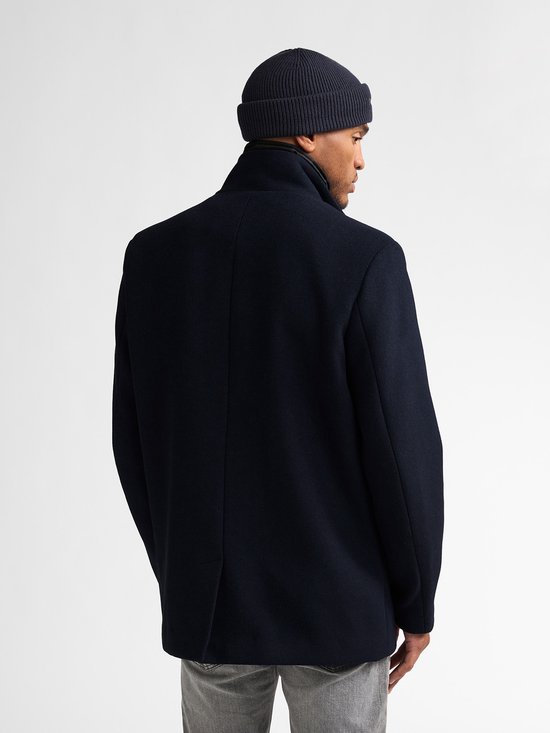 Model gezien vanaf de rug, dragend een marineblauwe wollen mantel en beanie.