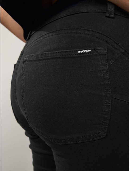 Detail van de achterzak van een zwarte jeans met een metalen label waarop 'NEXT' staat.