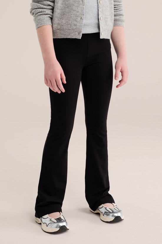 Model draagt een zwarte flared legging, gecombineerd met een grijze gebreide vest en zilverkleurige sneakers.
