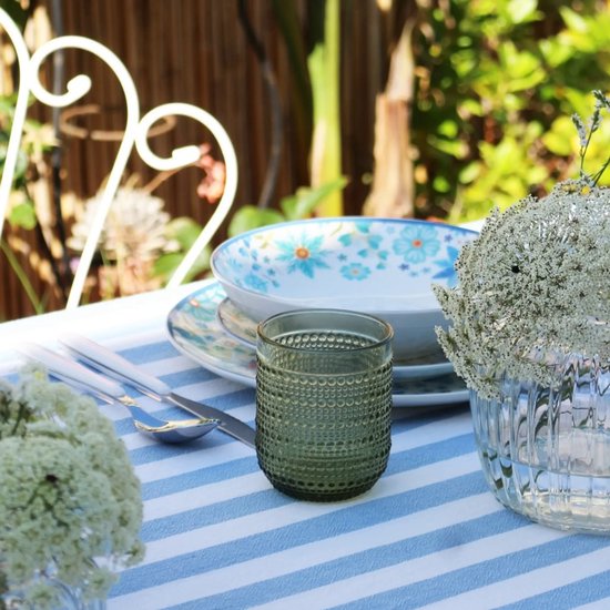 Donkergroen glas met bobbelig reliëf op een tafel met blauw gestreept tafelkleed en bloemstuk.