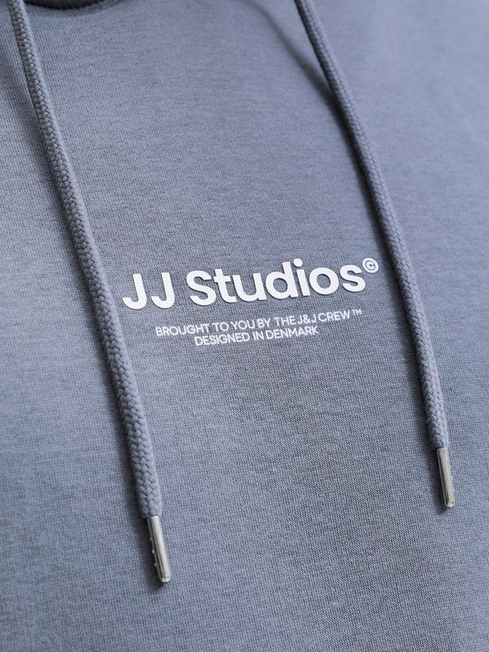 Close-up van de grijze hoodie met het 'JJ Studios' logo en de witte trekkoorden.