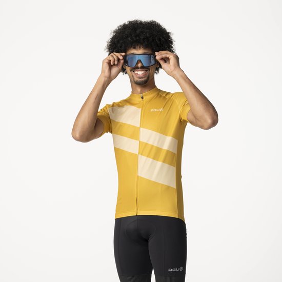 Man met afro draagt geel fietsshirt, met diagonale strepen, zwarte fietsbroek en zonnebril.