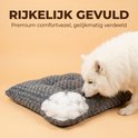 Witte hond snuffelt aan een grijs hondenkussen.