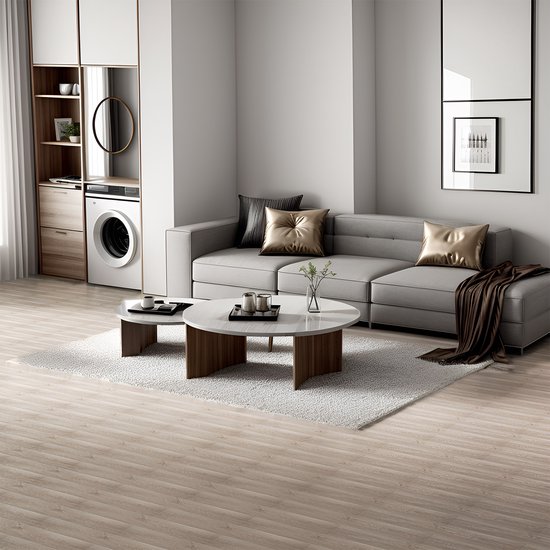 Woonkamer met lichte houten vloer, grijze bank en ronde salontafel op een wit kleed.