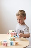 Jongen met blond haar speelt met gekleurde blokken met letters. Hij zet een blok met de letter 'u' op een stapel.