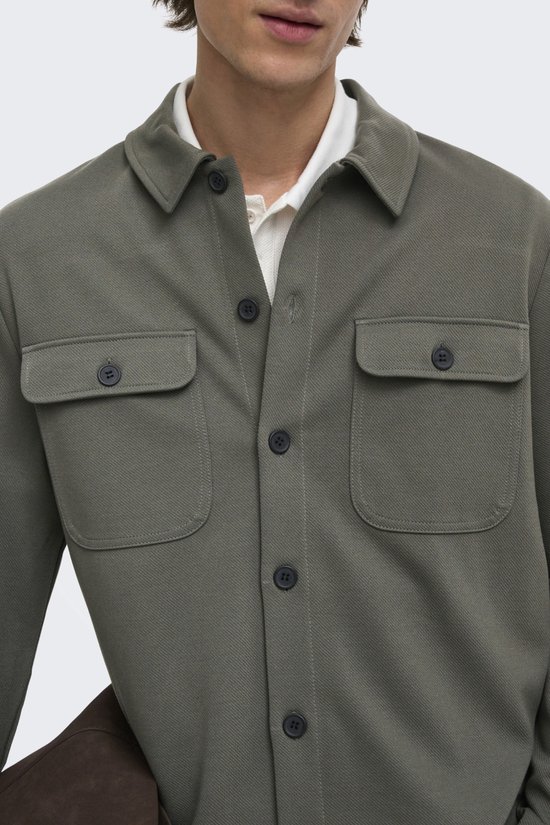 Close-up van een middengrijs shirtjack met twee borstzakken en donkere knopen.