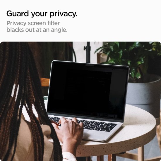Een vrouw met lange vlechten zit aan een tafel en gebruikt een laptop met een privacy screen protector.