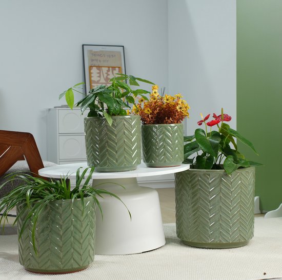 Vier groene keramieken bloempotten met visgraatpatroon, gevuld met planten, op een tafel.