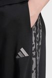 Close-up van een zwarte joggingbroek met het adidas-logo en een luipaardprint zijstreep.