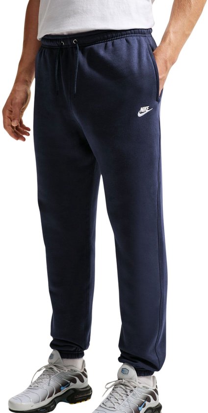 Man met de hand in de zak van een donkerblauwe Nike joggingbroek.