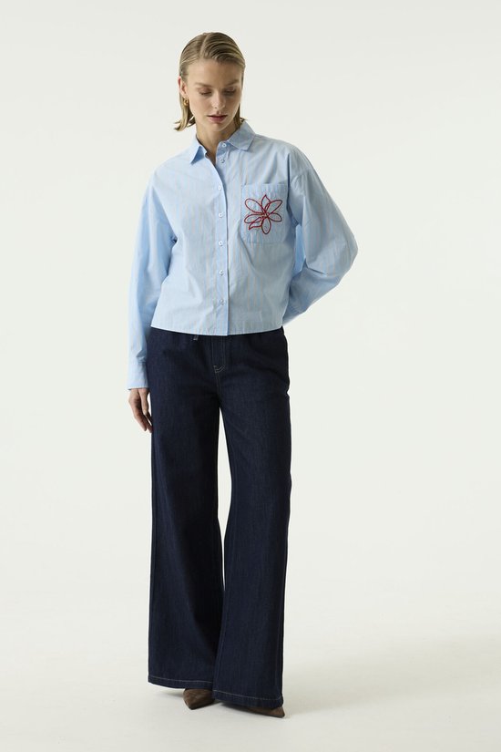 Model draagt een lichtblauw gestreept overhemd met rode bloemenprint en een donkerblauwe wide fit jeans.