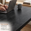 Close-up van het zwarte, verweerde tafelblad van een bureau met een laptop.