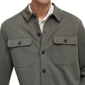 Mannelijk model draagt een olijfgroene, lange mouwen oversized shirt met twee borstzakken en donkere knopen.