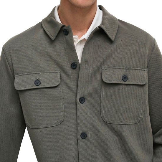Mannelijk model draagt een olijfgroene, lange mouwen oversized shirt met twee borstzakken en donkere knopen.