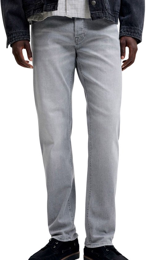 Man met grijze jeans, staand met handen in de zakken.