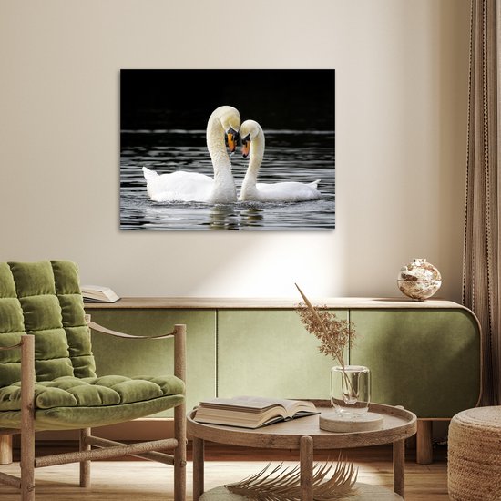 Deux cygnes blancs au bec orange nagent dans l'eau sombre, leurs cous forment un cœur, accrochés au mur dans un salon.