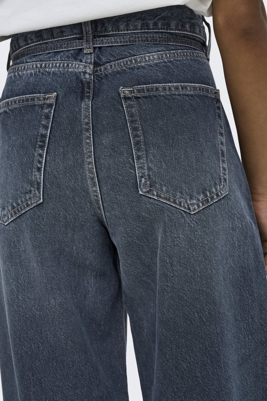 Model in wit shirt en donkerblauwe wijde jeans met strikceintuur, van voren gezien. De jeans hebben een stonewashed uiterlijk.