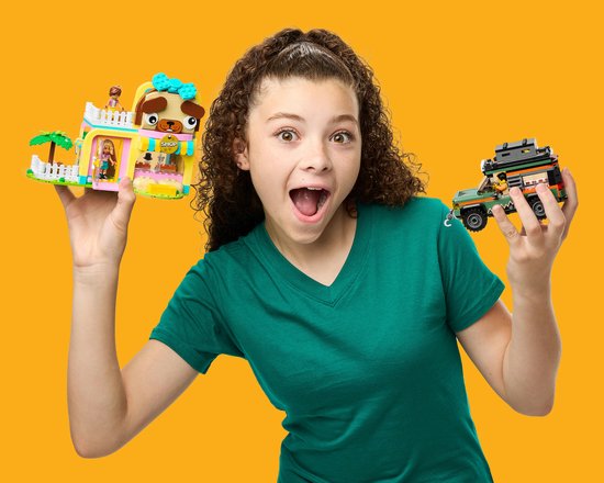 Fille aux cheveux bouclés en t-shirt vert tenant une animalerie rose et une jeep, toutes deux en LEGO.