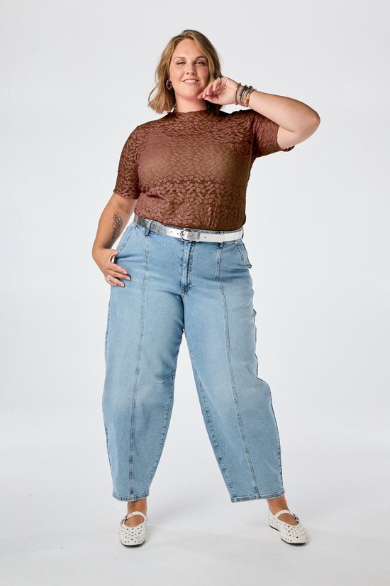Vrouw in bruine kanten top, jeans en witte riem.