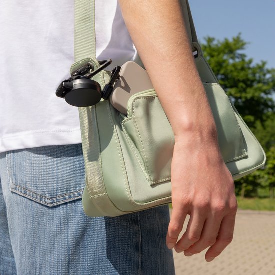 Lichtgroene crossbodytas met een telefoon en een zwarte kabel met karabijnhaak aan de buitenkant.