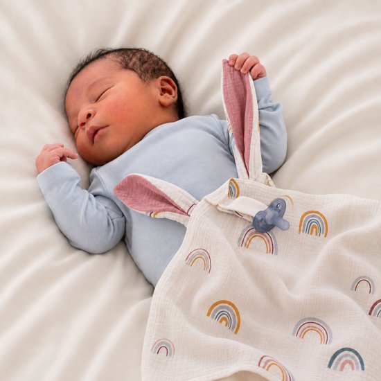 Baby met blauw rompertje en speendoekje met regenboogprint en konijnenoren.