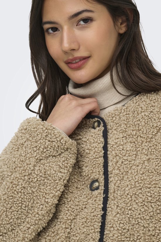 Model draagt een bruine teddy jas met zwarte biezen en knopen. Ze draagt ook een coltrui.