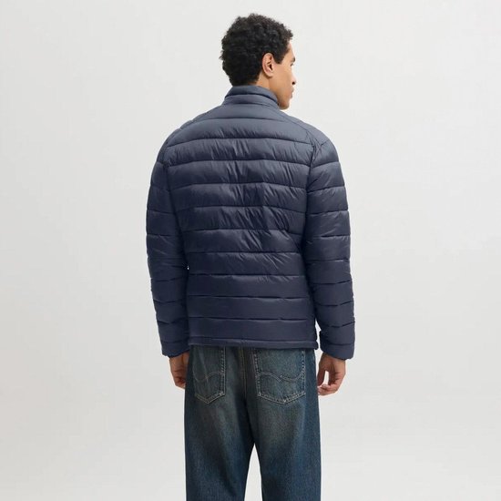 Model van achteren gezien in een donkerblauwe, doorgestikte pufferjas en spijkerbroek.