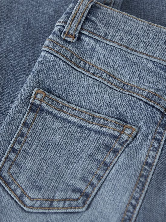 Detail van de achterzak van een lichtblauwe spijkerbroek, met stiksels en coin pocket.