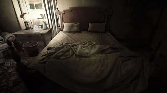 Een rommelig bed met witte lakens in een donkere slaapkamer met een nachtkastje en lamp.