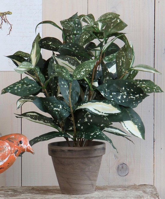 Groene kunstplant met witte spikkels, in een grijze pot, naast een oranje vogeldecoratie.