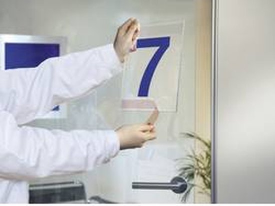 Handen bevestigen een nummer '7' op een glazen deur met dubbelzijdige tape.