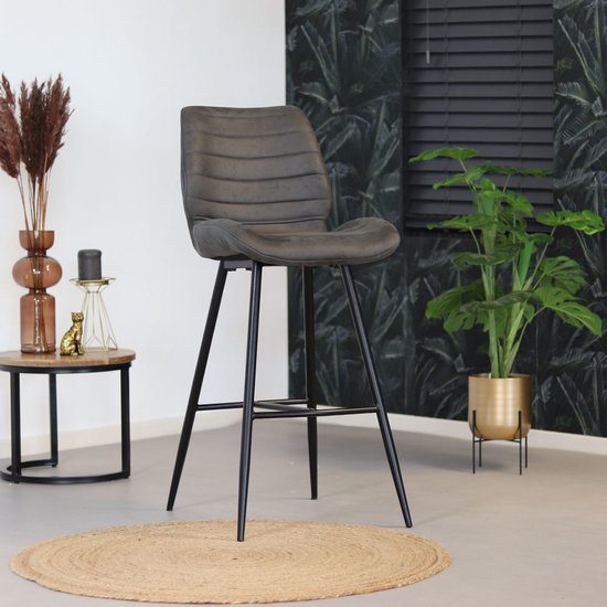 Antracietkleurige barkruk met horizontale stiksels, zittend op een jute mat in een tropisch interieur.