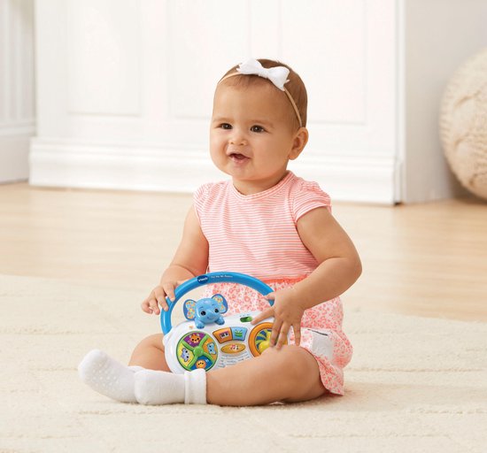 Een baby zit op de grond met een witte muziekradio met blauwe handvat, blauwe olifant en gekleurde knoppen.