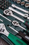 Close-up van ratelsleutels, een moersleutel en een schroevendraaier met groene handvatten in een gereedschapskoffer.