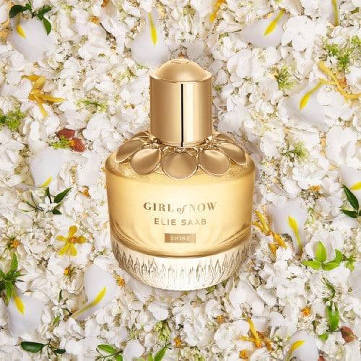 Gouden parfumfles met gegolfde glazen bodem, gouden dop en bloemendecoratie. Tekst: GIRL of NOW, ELIE SAAB, SHINE.