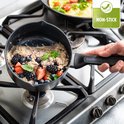 Une main tient une casserole de flocons d'avoine et de baies au-dessus d'une cuisinière à gaz. Logo "NON-STICK".