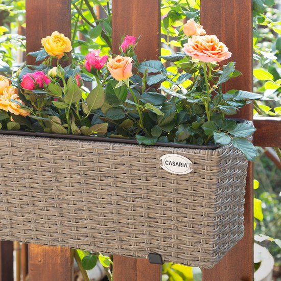 Beige plantenbak met gevlochten textuur, hangend aan een houten hek, gevuld met roze en gele rozen.