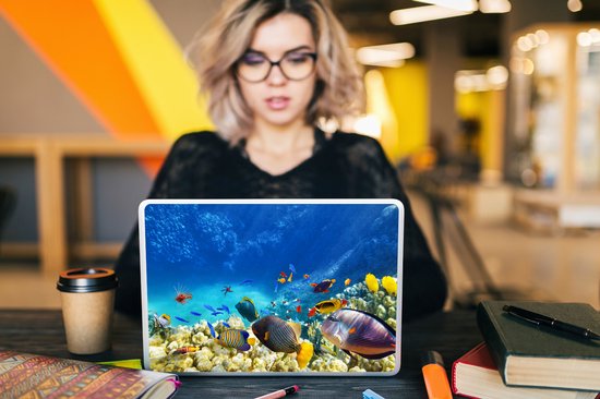 Ordinateur portable avec autocollant monde sous-marin : coraux, poissons et poisson-lion, près d'une femme au travail.