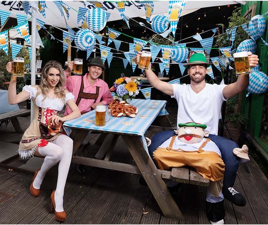 Vier personen op een picknicktafel, met bier, pretzels en versieringen. De mannen dragen traditionele Duitse kleding.