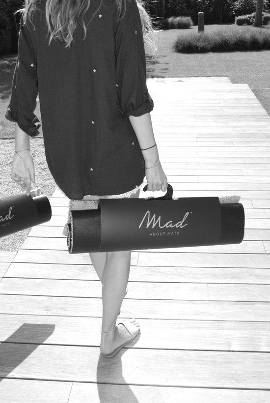 Femme portant une blouse foncée à étoiles, se déplace avec un tapis dans un sac de transport noir mat de Mad About Mats.