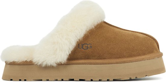 Cognackleurige UGG slipper met dikke crèmekleurige schapenwolvoering aan de zijkant. De slipper heeft een dikke, beige zool.