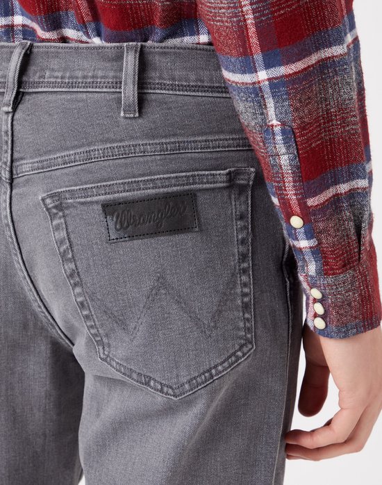 Close-up van de achterkant van een grijze jeans met een zwart Wrangler-label op de rechterzak.