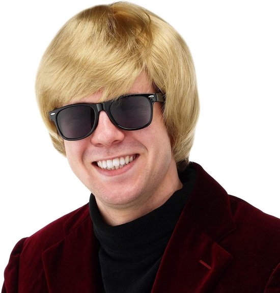 Man met blond kapsel en zwarte zonnebril, lach met witte tanden, zwarte coltrui en bordeauxrode blazer.