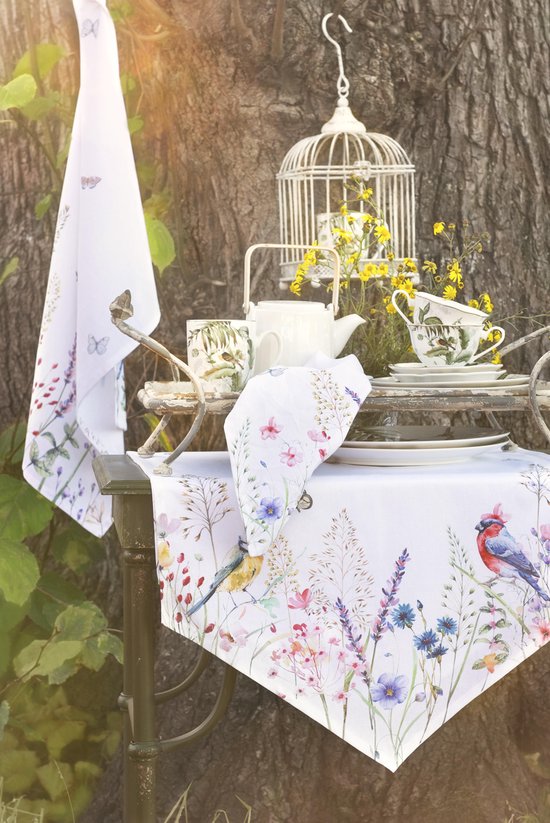 Een witte theedoek met vlinders en bloemen, bij een vogelkooi en servies buiten.