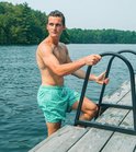 Jongeman met zwemshort met mozaïekpatroon in mintgroen en blauw, klimt op een ladder uit het water.