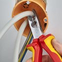 Hand gebruikt rode en gele tang om witte kabel te snijden in oranje elektriciteitsdoos.