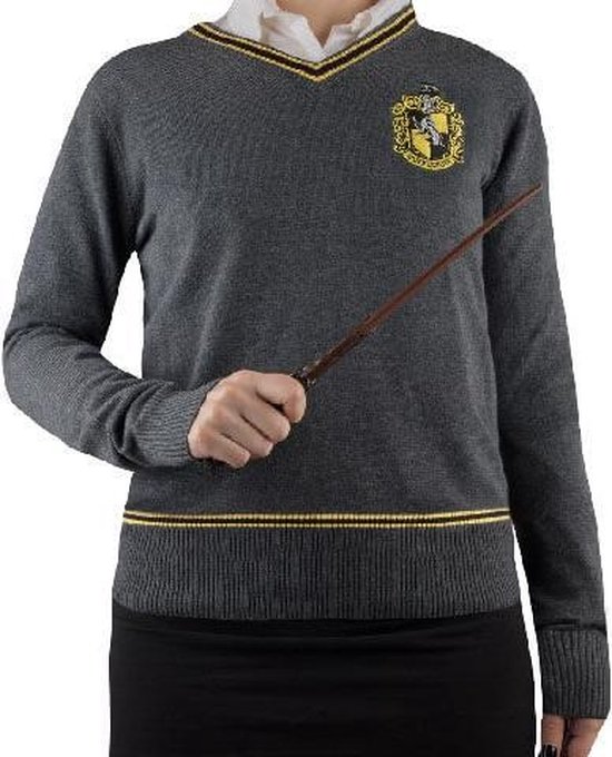 Grijze V-hals trui met geel en zwart gestreepte boorden en kraag. Hufflepuff wapenschild op linkerborst. Model houdt toverstok vast.