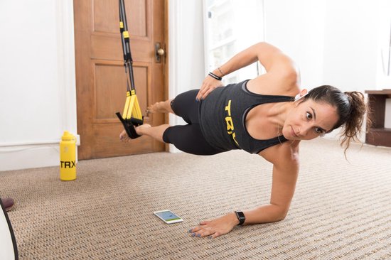 Vrouw die een zijwaartse plankoefening doet met de TRX-trainingsbanden, met een waterfles op de grond.