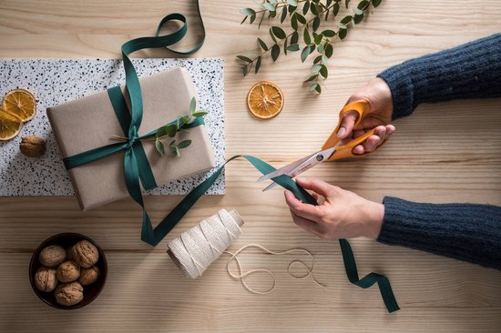 Handen gebruiken oranje Fiskars schaar om een groen lint te knippen voor een cadeau.